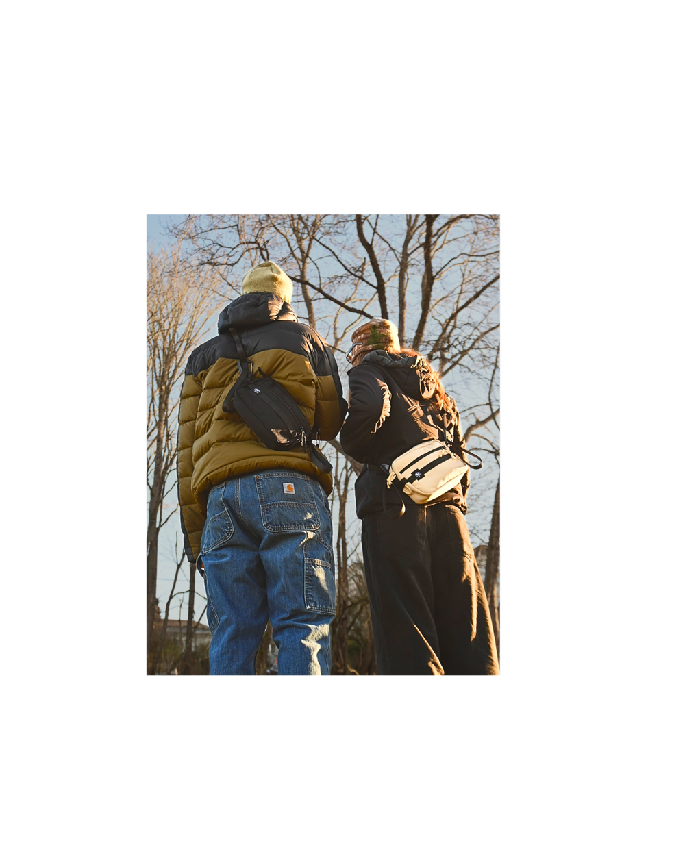 Two people walking away from the camera with backpacks, surrounded by leafless trees.
